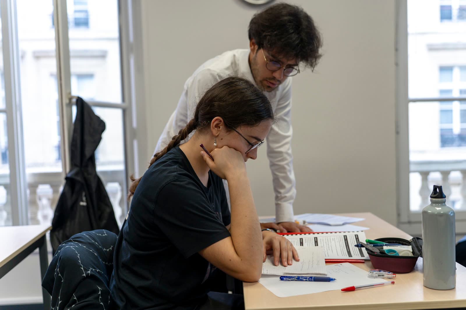 Un mentor se penche vers une élève qui suit les explications sur sa feuille.