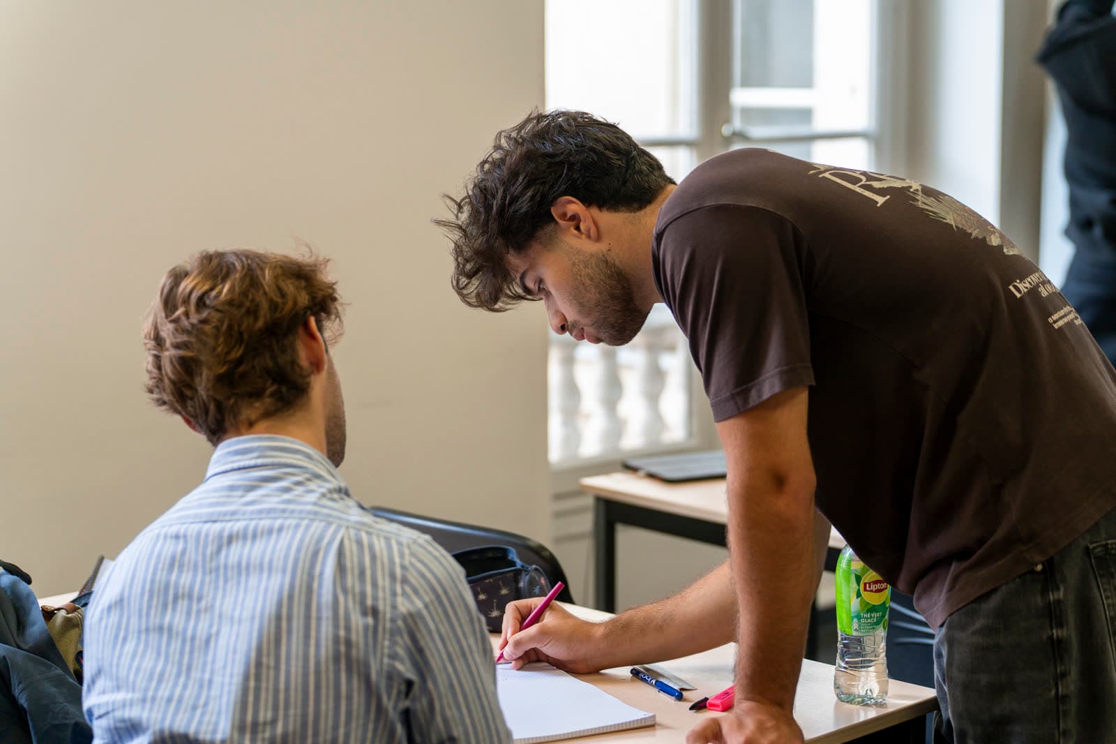 Un mentor corrige une copie posée sur la table devant un élève.